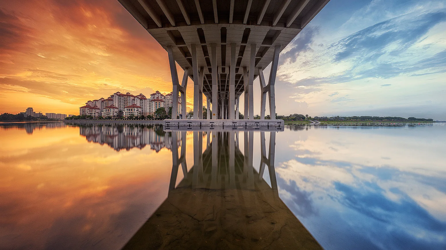 Still water beneath a bridge at sunset, the structure doubled in the reflection