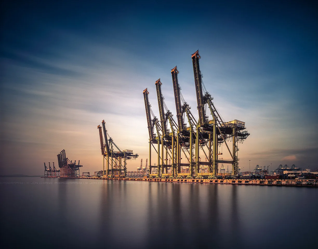 Gantry cranes standing off in haze, water gone to glass.