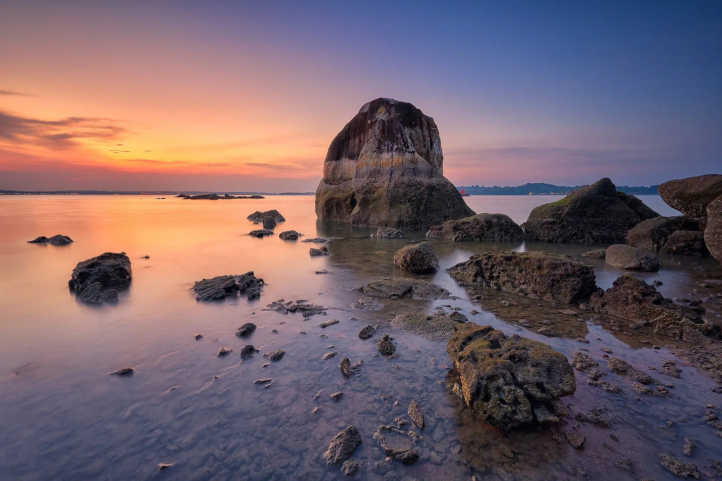Long exposure smoothing the water around a weathered outcrop at dusk.